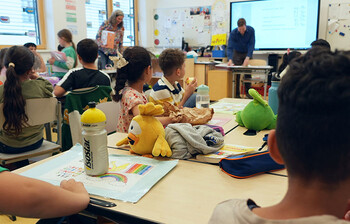 Schulkinder sitzen in einem Klassenzimmer und hören dem Lehrer vorne zu.