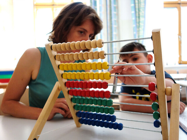 Ehrenamtliche übt mit einem Kind Mathematik am Abakus im Klassenraum