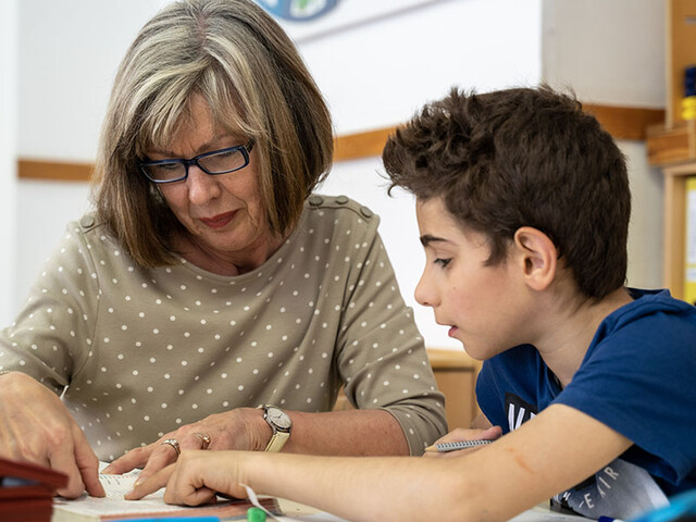 Ehrenamtliche erklärt einem Schüler den Lernstoff im direkten Gespräch am Tisch