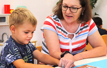 Ehrenamtliche unterstützt einen Jungen spielerisch beim Lernen am Tisch