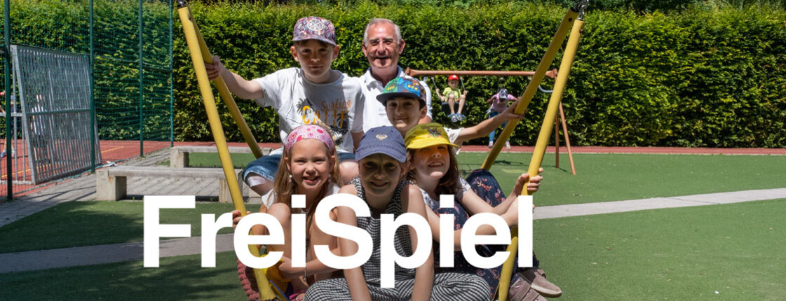 Freiwilliger schaukelt mit einer Gruppe lachender Kinder auf einem Spielplatz