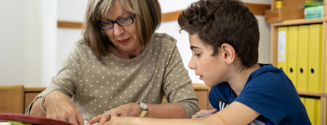 Freiwillige erklärt einem Schüler den Lernstoff im direkten Gespräch am Tisch
